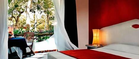 A bedroom with a bed, a nightstand, a table with chairs, and a view of a garden.