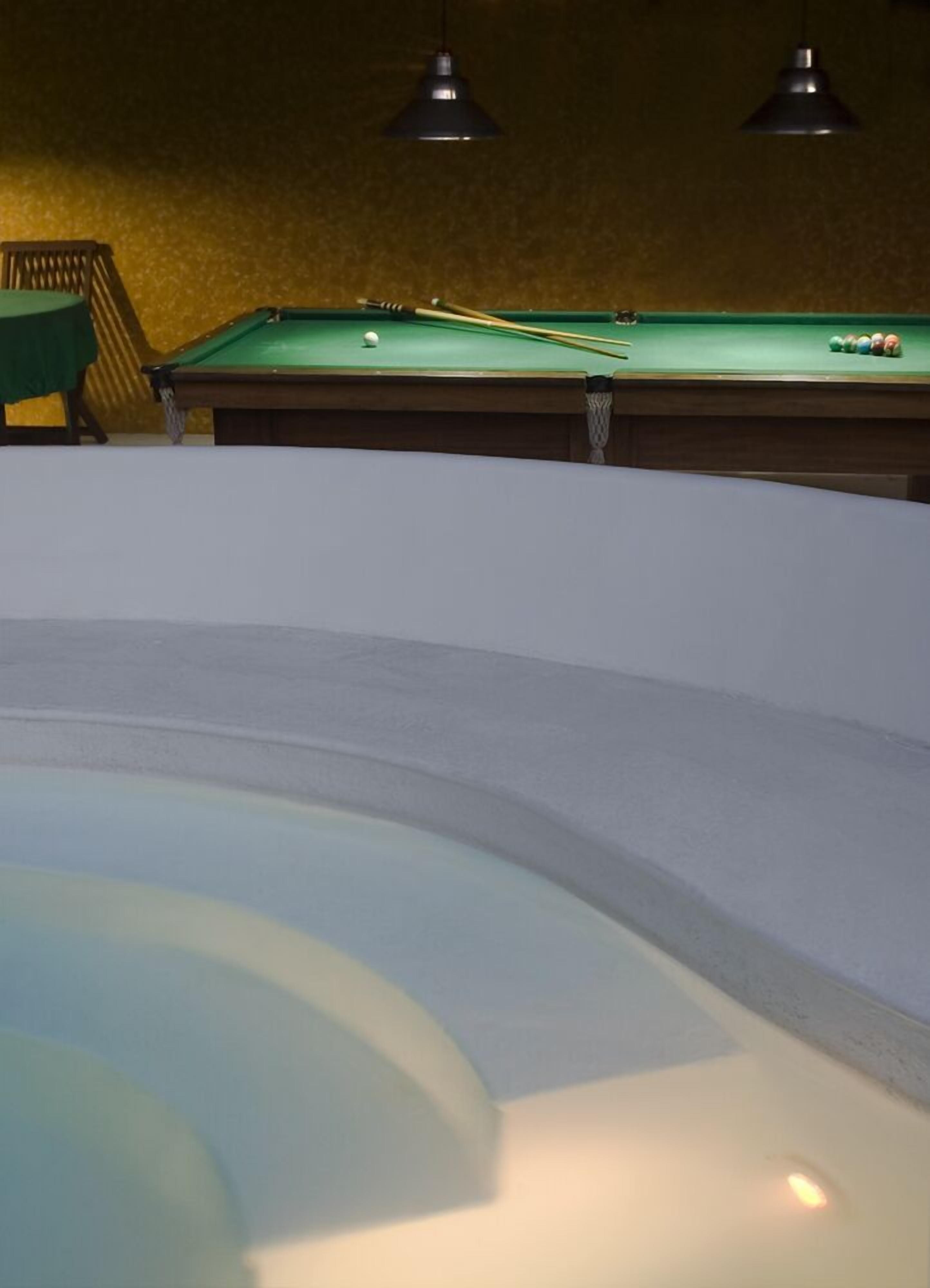Una mesa de billar con superficie de fieltro verde, una vara y bolas de billar.