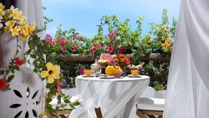 A table set outdoors with a variety of fruits and beverages, surrounded by lush greenery and flowers. - My Blue Hotel (Jijoca de Jericoacoara)