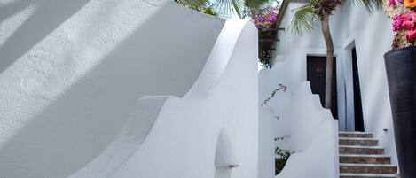 Un edificio blanco con fachada curva, una escalera que lleva a una puerta y una maceta grande con flores rosas.