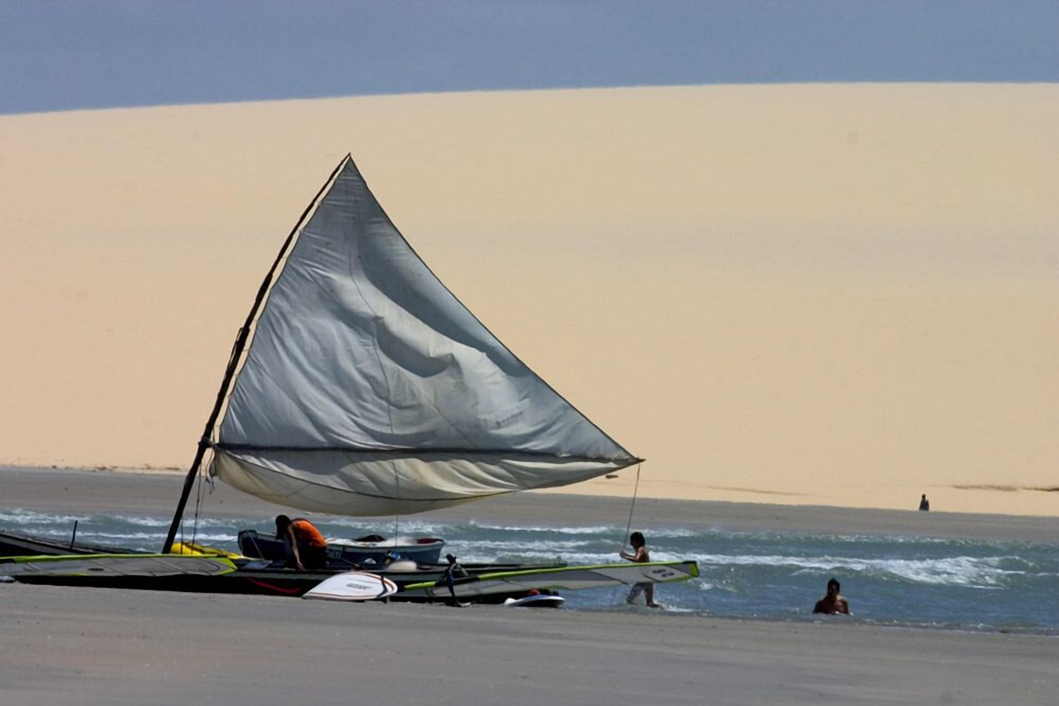 A beach with a sailboat and people in the water.