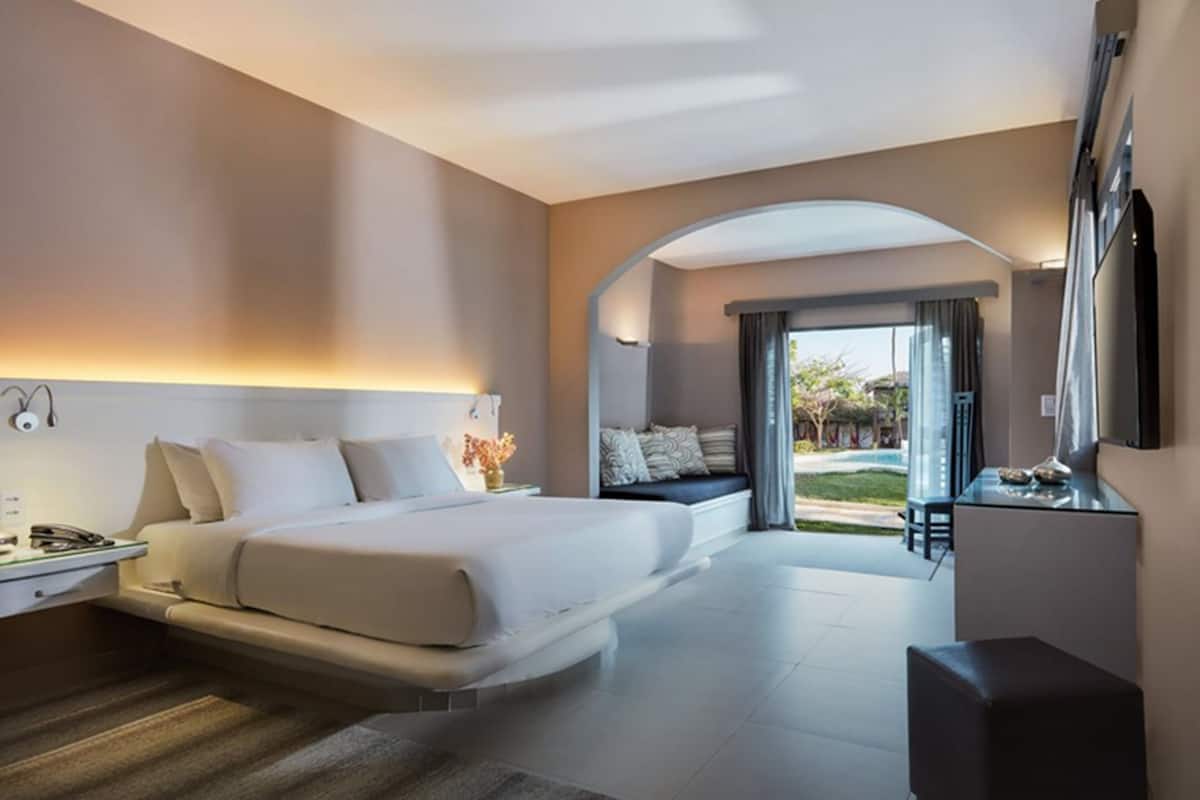 A modern hotel room with a large bed, a desk, and a view of the outdoors.