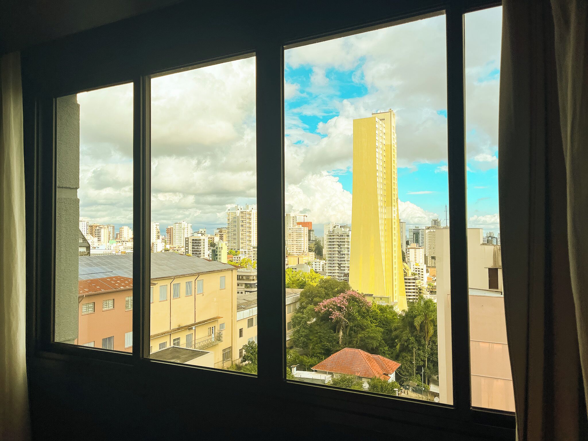 Una ventana con vistas a un paisaje urbano, incluyendo un edificio amarillo alto y varios edificios más.