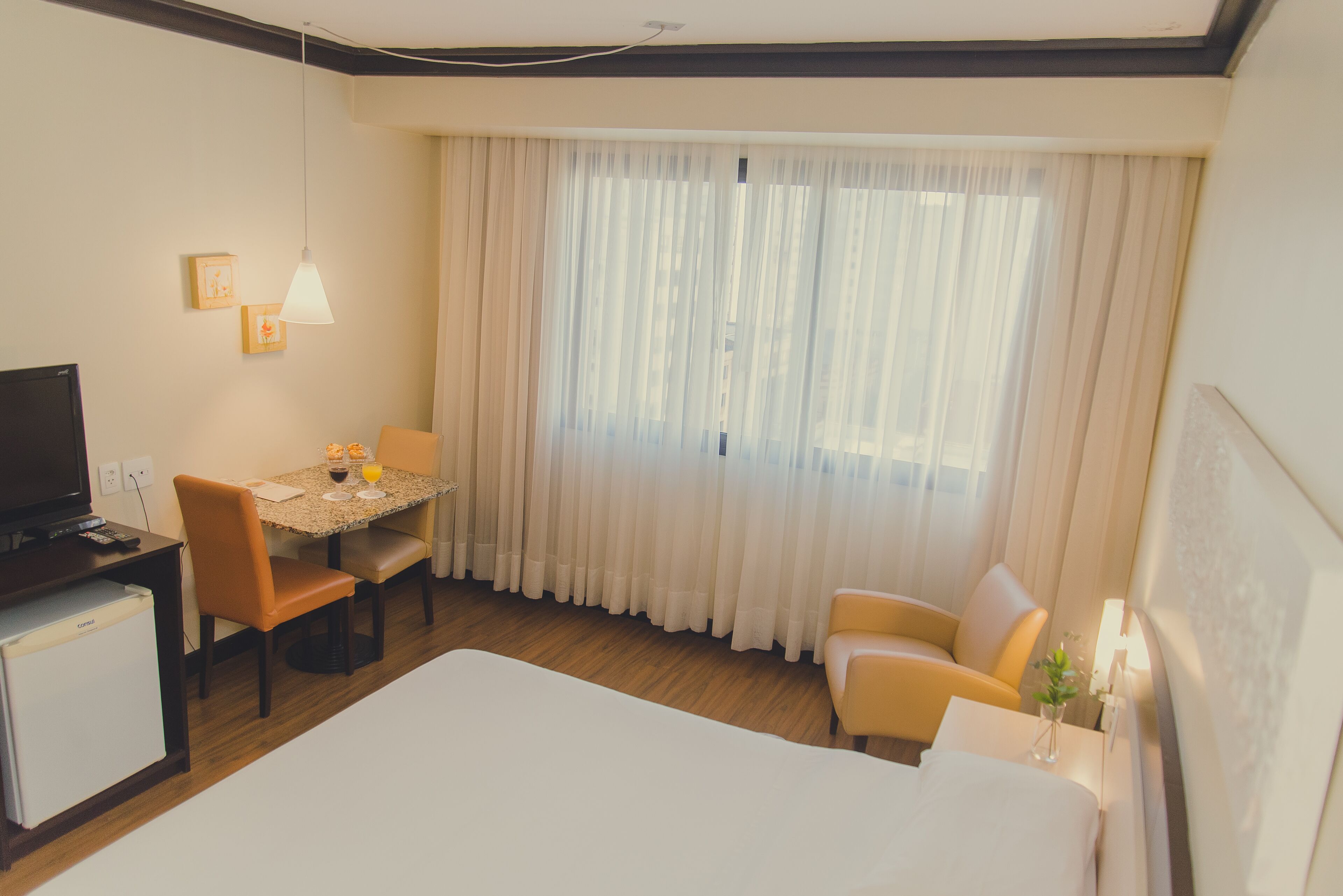 Habitación de hotel con cama, escritorio con silla, televisión y ventana con cortinas.