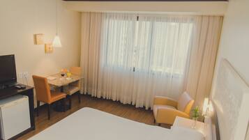 A hotel room with a bed, a desk with a chair, a television, and a window with curtains.