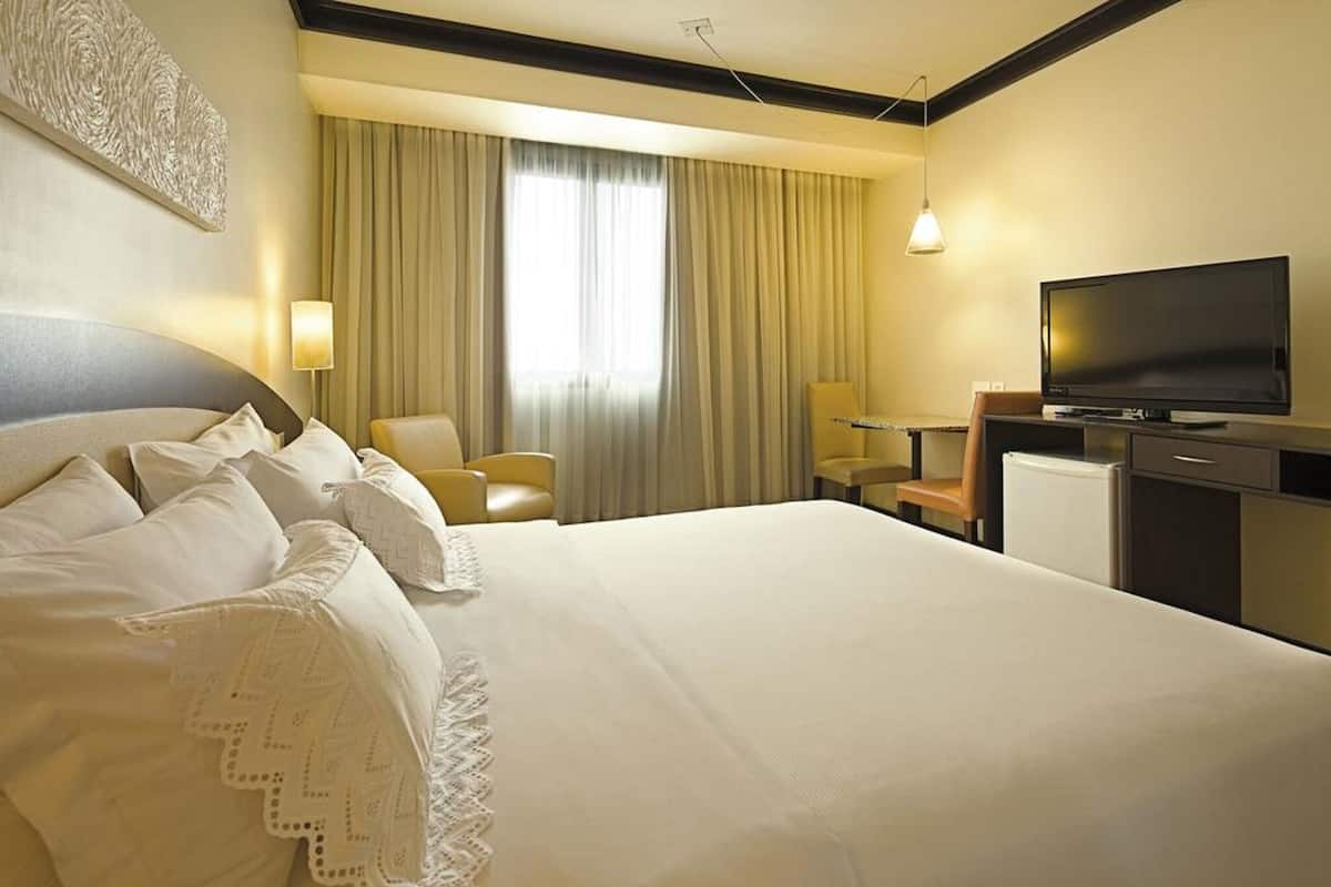 Una habitación de hotel con una cama grande, televisión, escritorio y una silla.