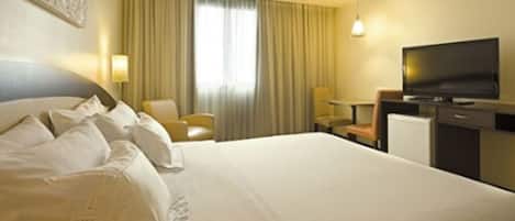 A hotel room with a large bed, a television, a desk, and a chair.