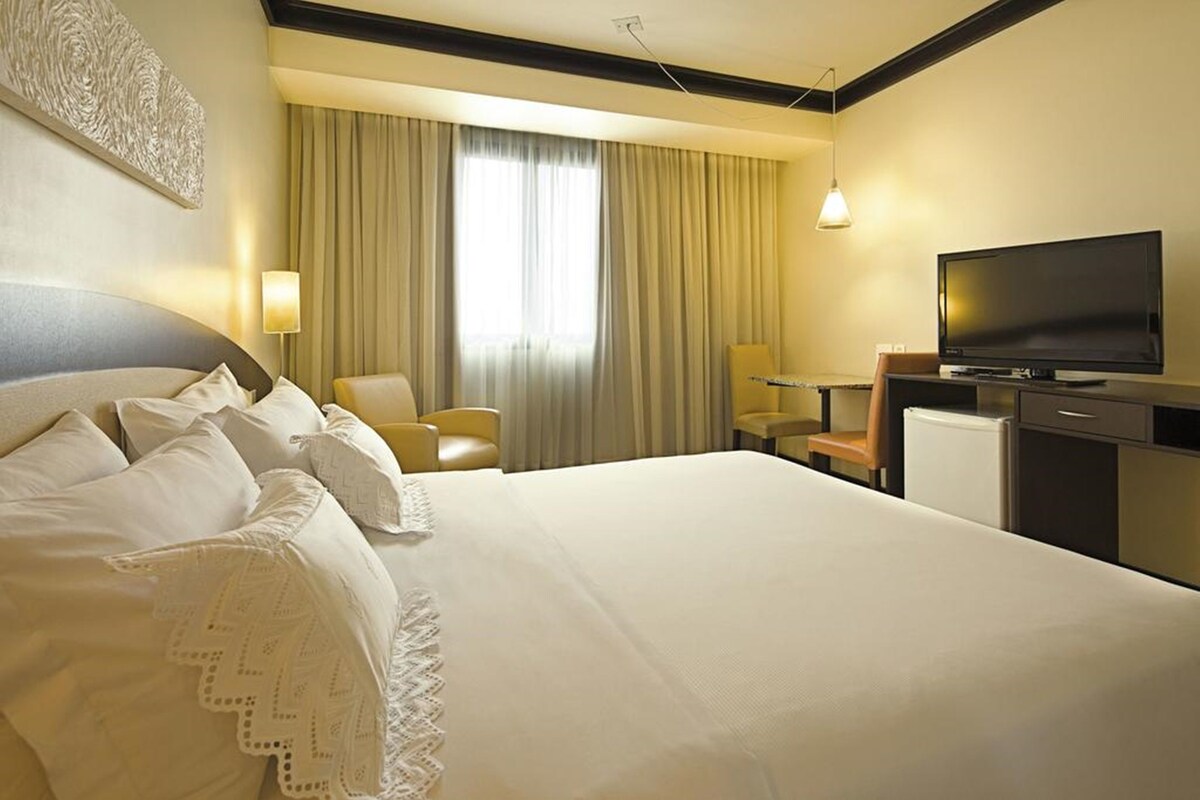 A hotel room with a large bed, a television, a desk, and a chair.