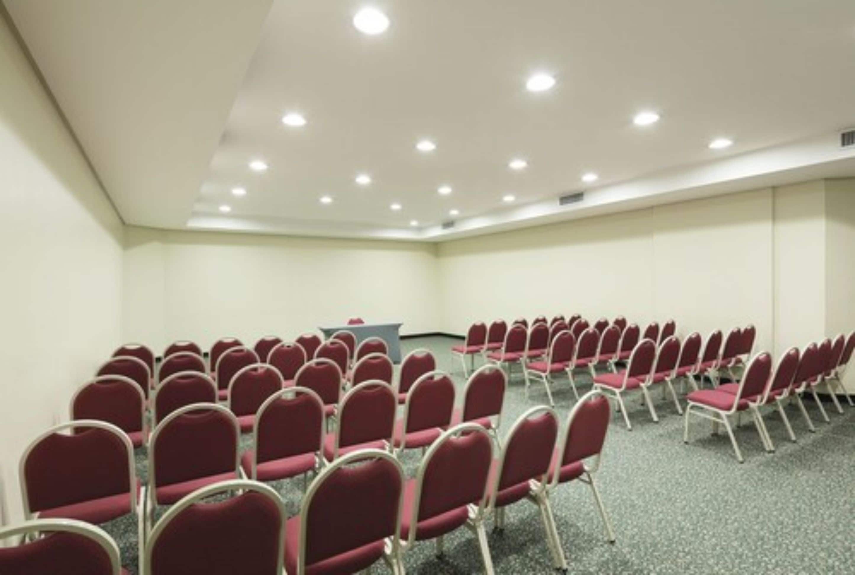 A conference room with rows of red chairs, a podium, and a carpeted floor.