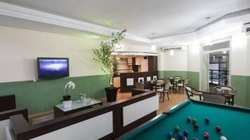 A pool table with balls, a reception desk, a television, and a seating area with chairs and tables.