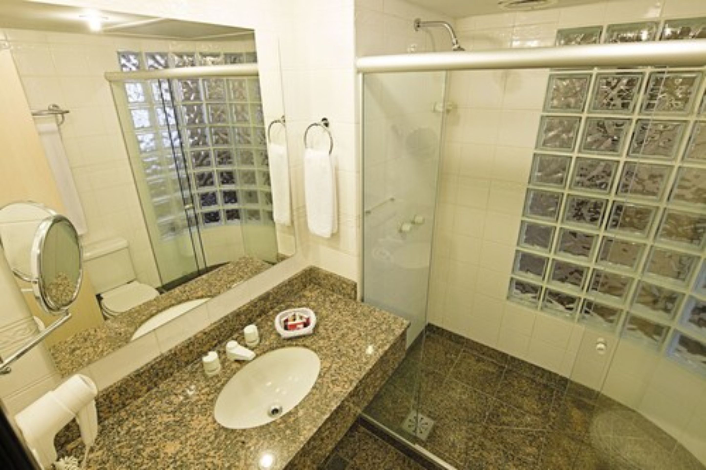 Un baño con encimera de granito, lavamanos, cabina de ducha de vidrio y pared revestida con mosaicos.