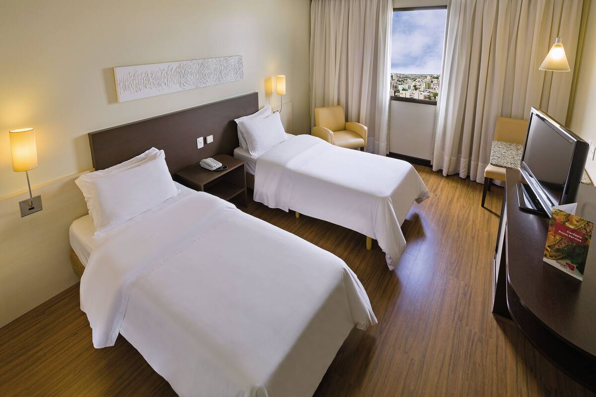 Habitación de hotel con dos camas, un escritorio, una silla, un televisor y una ventana con cortinas.