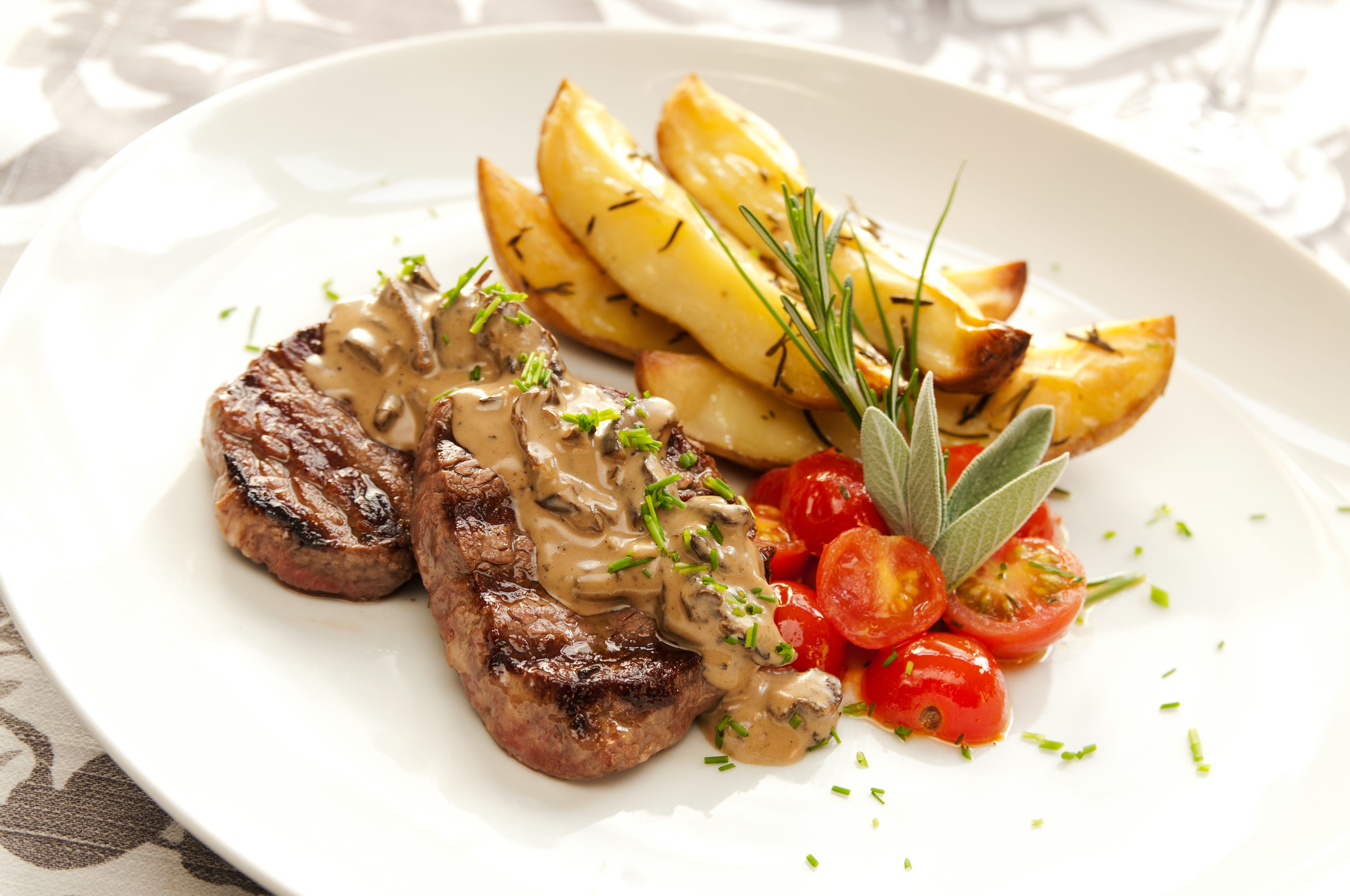 Un plato con bistec a la parrilla, patatas asadas, tomates cherry y una guarnición de hierbas.