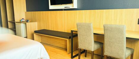 A hotel room with a bed, a desk with two chairs, a television, and a small refrigerator.
