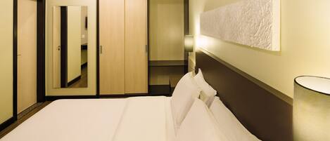 Habitación de hotel con una cama grande, un armario, un espejo y una lámpara fijada a la pared.