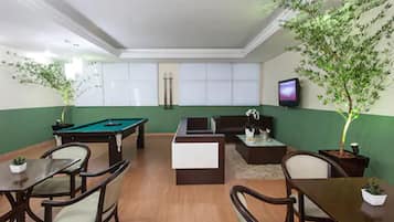 A room with a pool table, a sofa, a coffee table, and two potted plants.