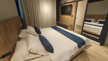 A hotel room with a large bed, a TV mounted on the wall, and a mirror reflecting the bed.