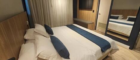 Una habitación de hotel con una cama grande, un televisor montado en la pared y un espejo que refleja la cama.