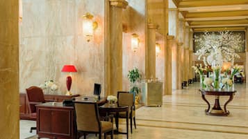 Un vestíbulo con paredes de mármol, una mesa de recepción y un área de estar con sillas y una mesa.