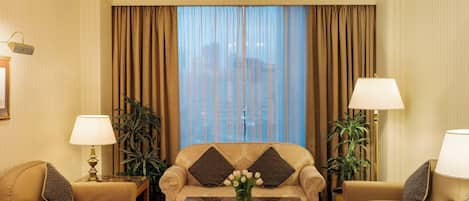 Habitación de hotel con un conjunto de sofá, dos lámparas, una araña y vistas a través de cortinas translúcidas.