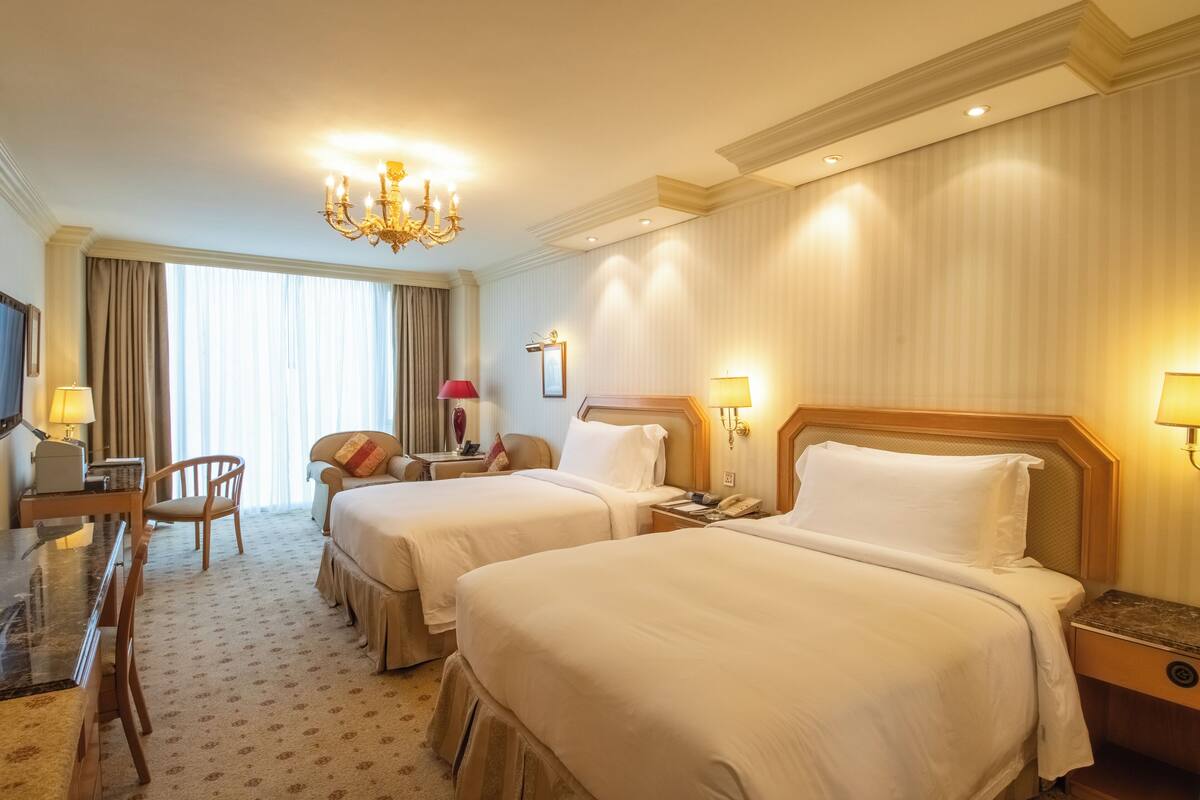 A hotel room with two beds, a desk, a chair, and a chandelier.