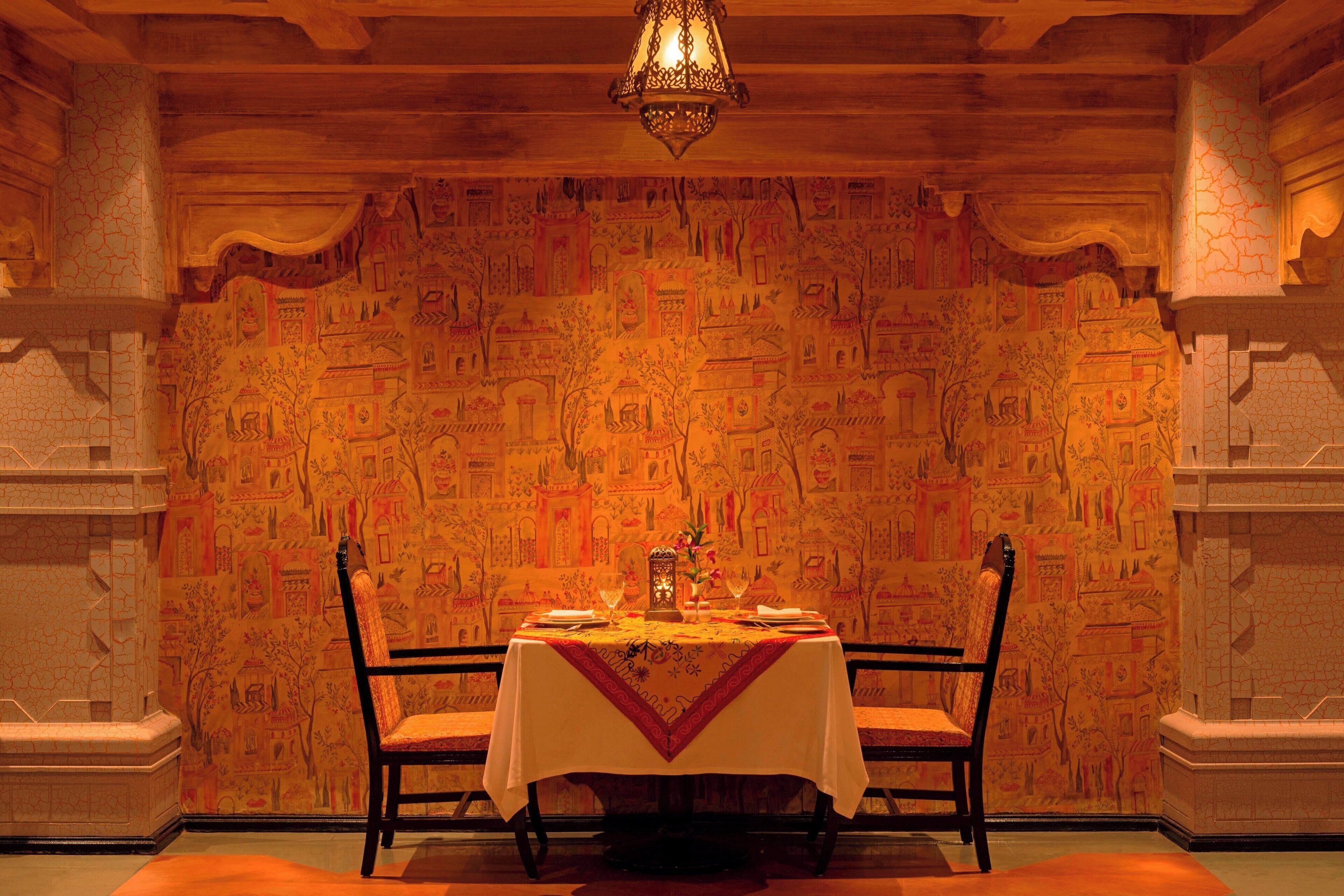 Un comedor con una mesa dispuesta para dos, una araña y una pared con diseños intrincados.