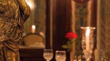 A golden statue on a pedestal, a table with a vase of red roses, and a chandelier in the background.