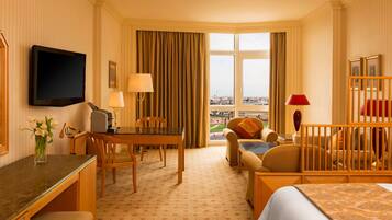 A hotel room with a bed, a desk, a chair, a table, a TV, a window with curtains, and a view of the city.