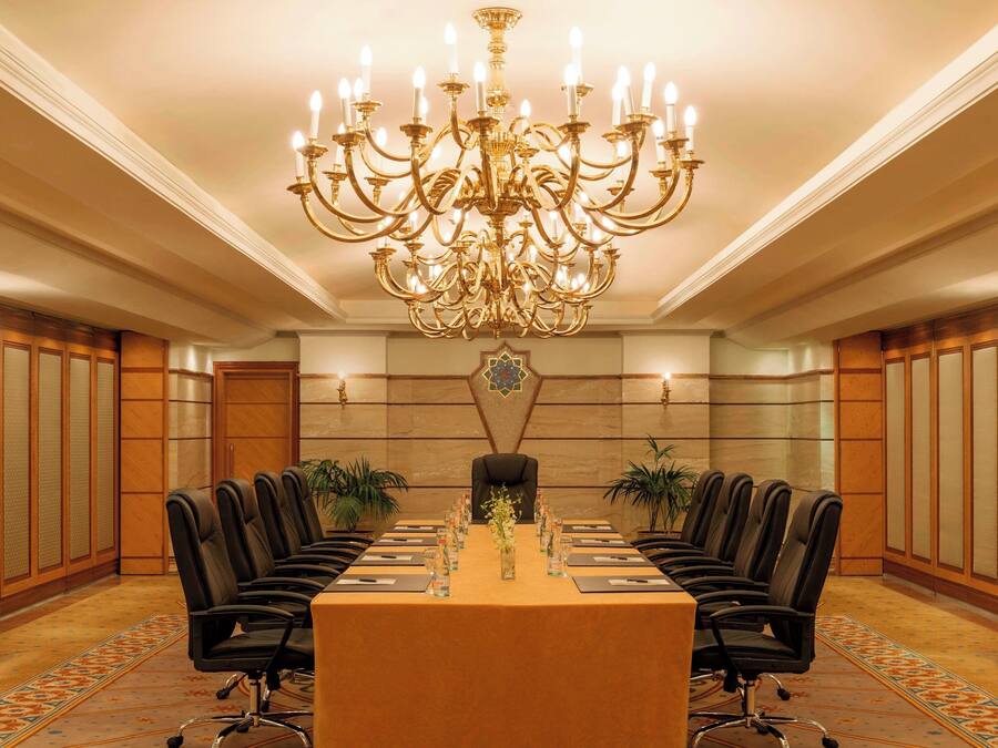 A conference room with a long table, black chairs, a chandelier, and potted plants.