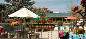 An outdoor patio area with green metal chairs, a white umbrella, and flower planters. - Foothills Inn (Rapid City)