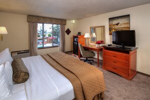 A hotel room with a bed, desk, TV, and a window with curtains.