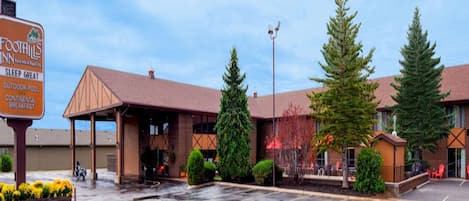 Un hôtel doté d’un espace extérieur couvert avec des sièges, d’une enseigne indiquant « FOOTHILLS INN » et proposant des équipements tels que « SLEEP GREAT », une « PISCINE EXTÉRIEURE » et un « PETIT-DÉJEUNER CONTINENTAL ».