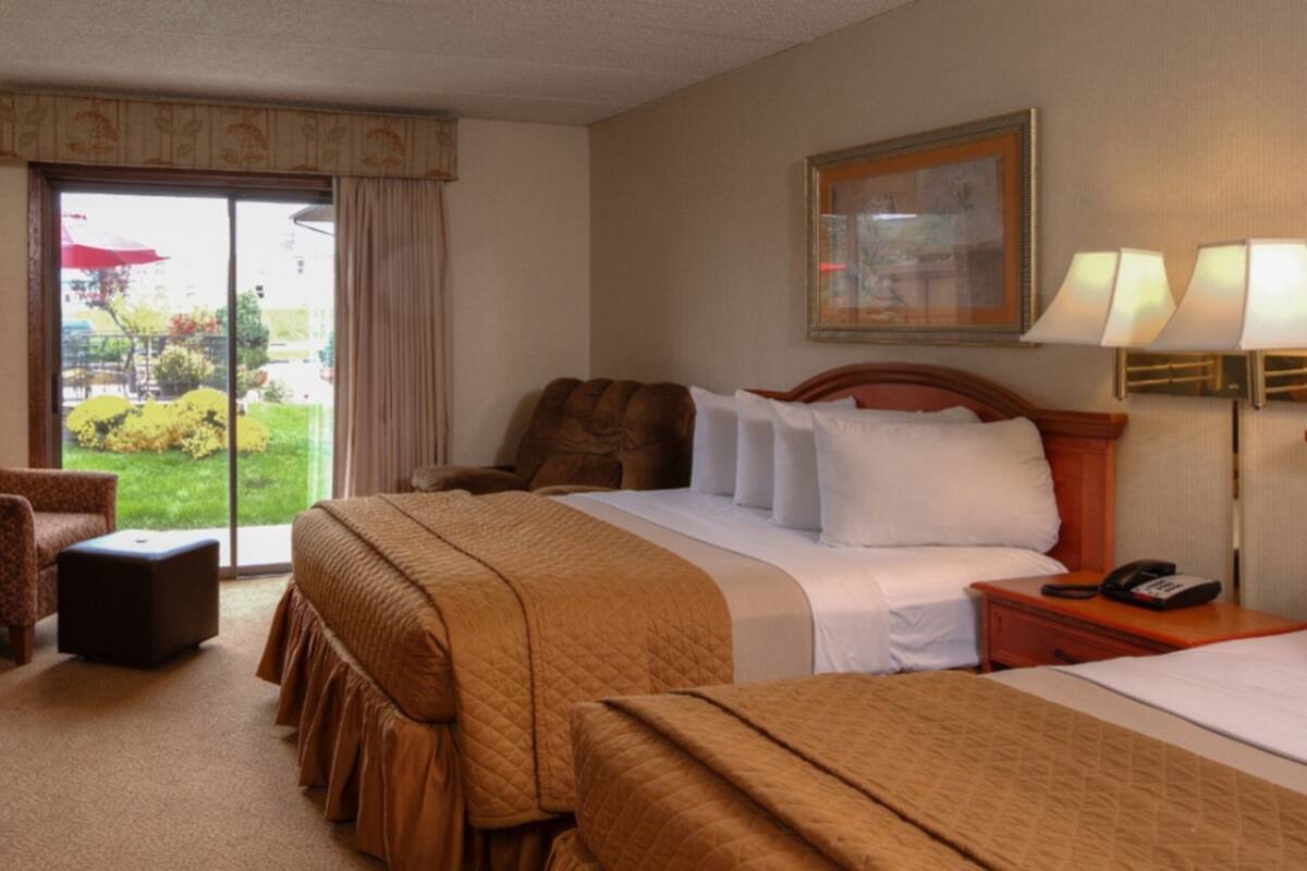 Une chambre d’hôtel avec un grand lit, une chaise, un bureau avec un téléphone et une fenêtre donnant sur l’extérieur.