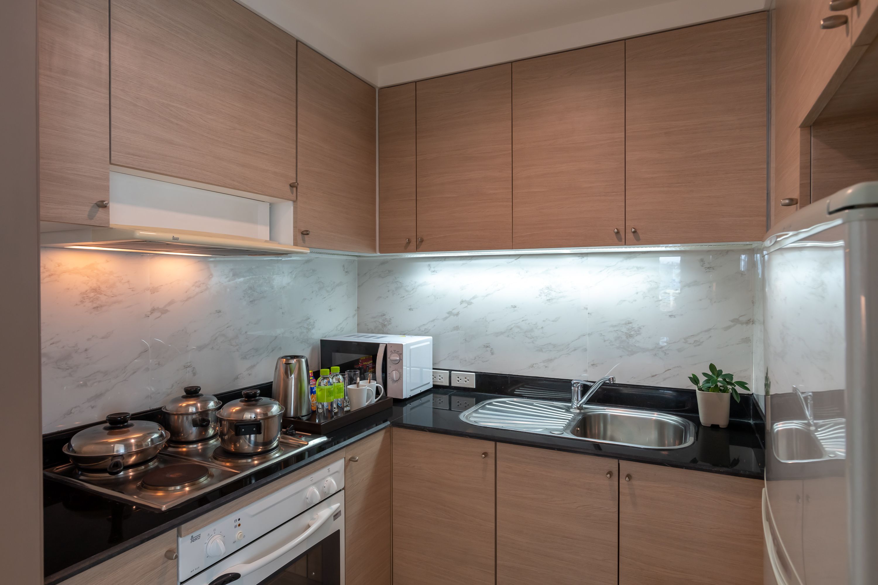 A modern kitchen with wooden cabinets, a black countertop, a stainless steel sink, and a built-in oven.