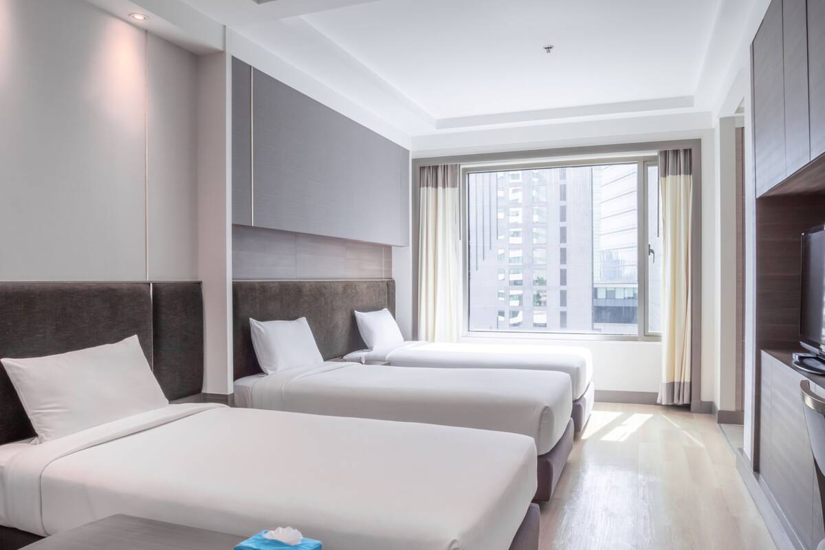 Habitación de hotel con dos camas, televisión y un ventanal con vistas a la ciudad.