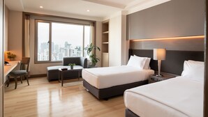 Une chambre d’hôtel moderne équipée de deux lits, d’un bureau, d’une chaise et d’une grande fenêtre donnant sur la ville.