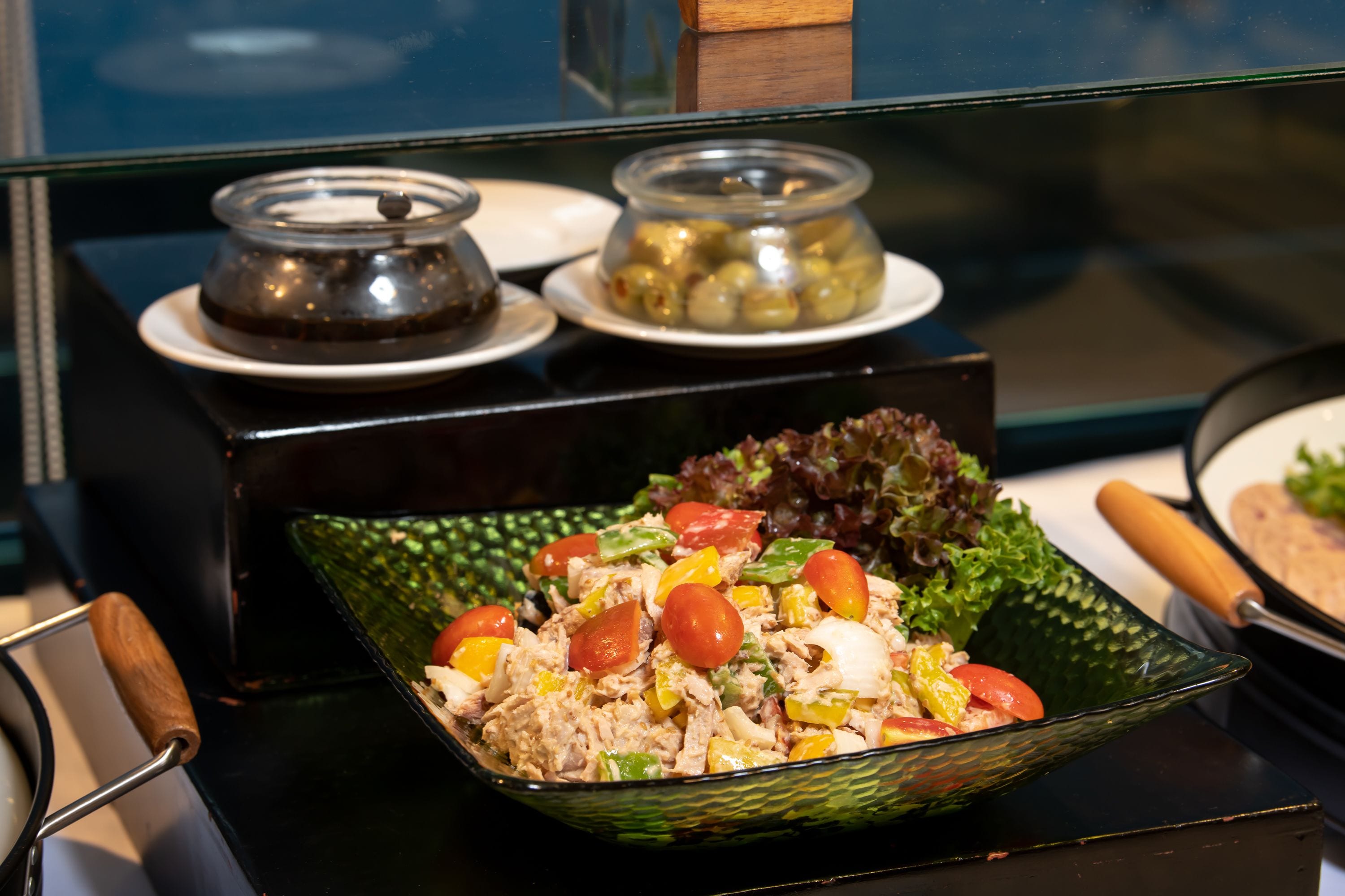 A buffet table with a variety of dishes including a salad, a bowl of olives, and a container of soup.