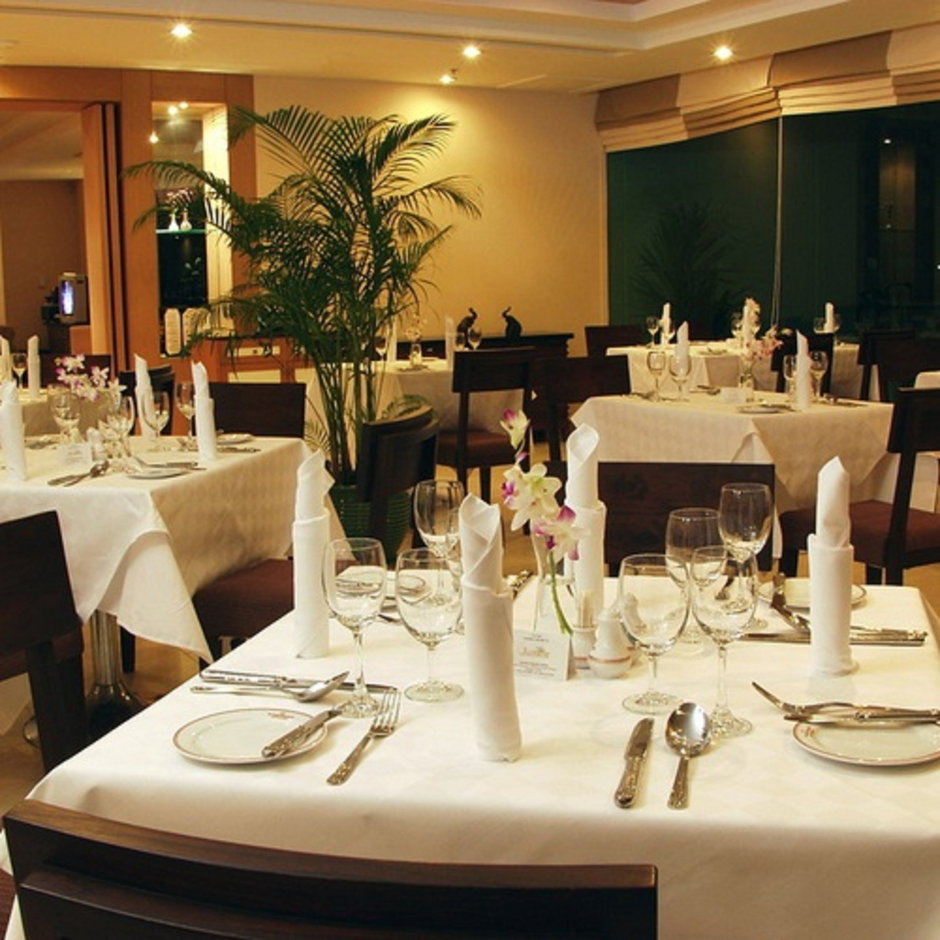 A restaurant with round tables set for dining, featuring white tablecloths, silverware, and glassware.