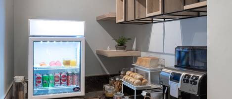 Un espacio de cocina compacto con refrigerador, cafetera y estantes para almacenamiento.