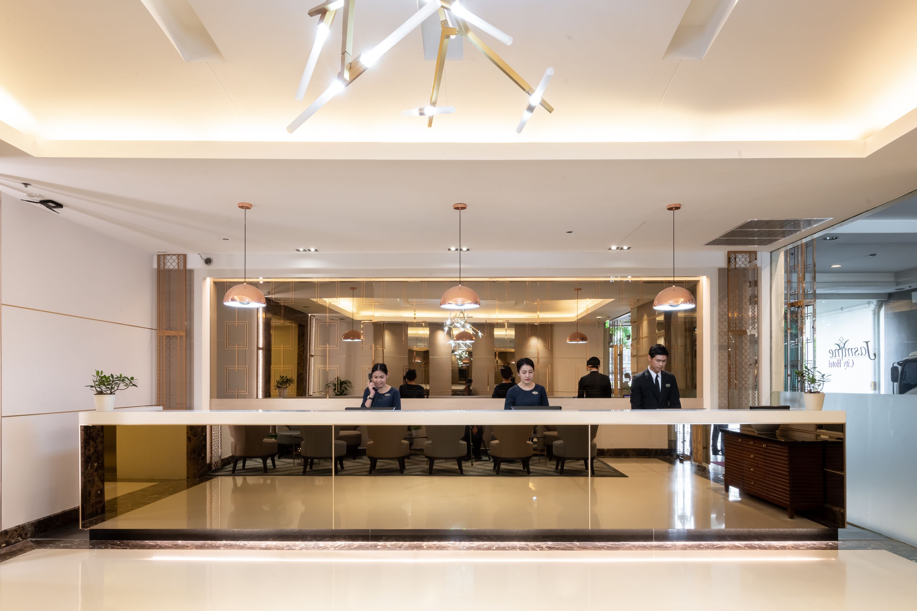 A modern hotel reception area with a long counter, several chairs, and a large chandelier.