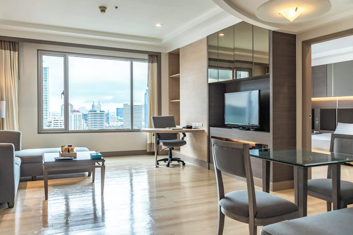 Una habitación de hotel moderna con un gran ventanal, un televisor de pantalla plana, una mesa de comedor de cristal y una zona de estar acogedora.