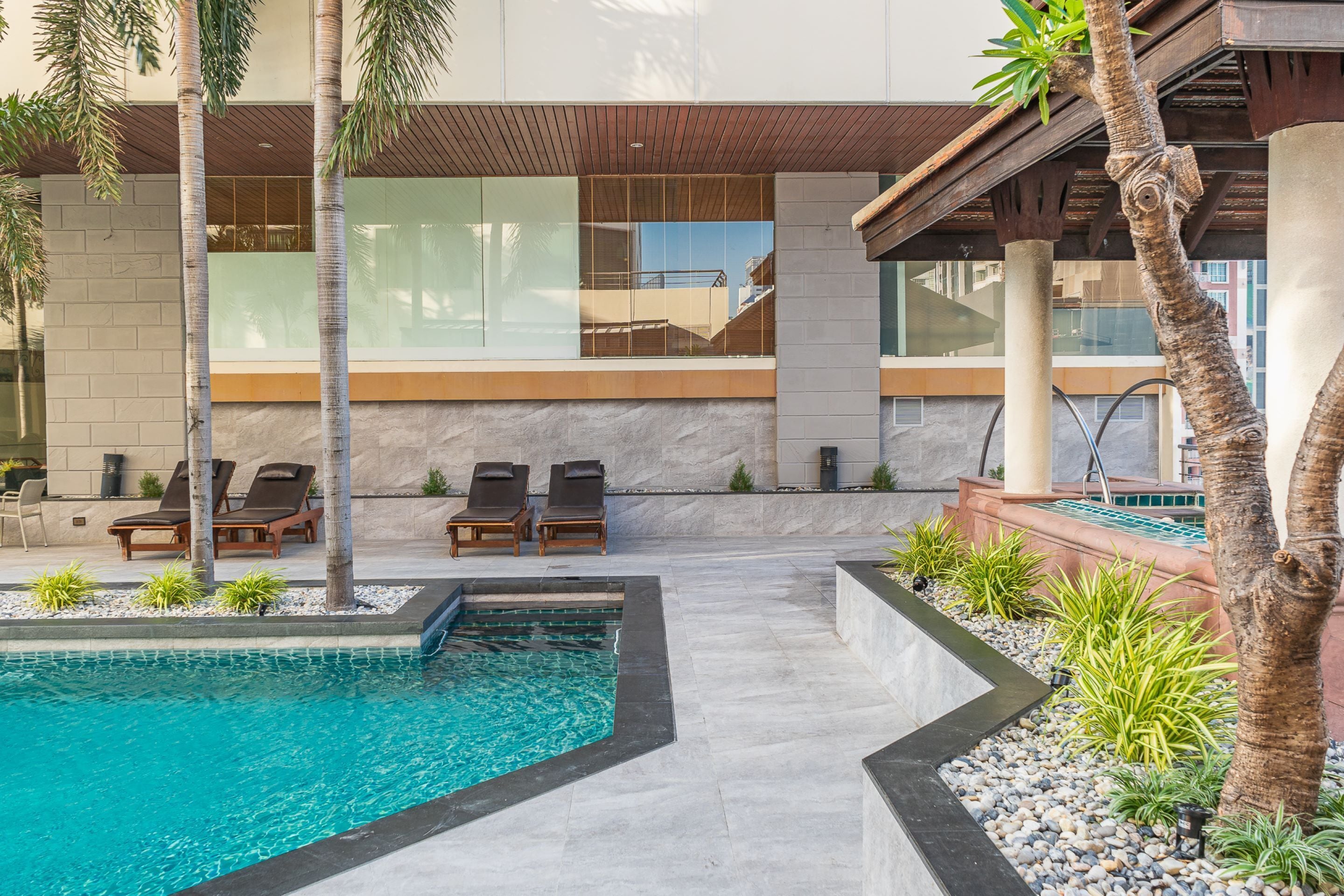 A modern outdoor pool area with lounge chairs, a stone wall, and a wooden pergola.