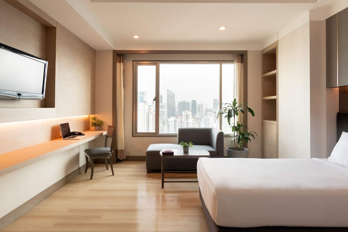 Una habitación de hotel moderna con vista a la ciudad, un escritorio, una silla, una cama y un televisor montado en la pared.