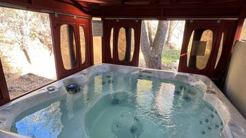 A hot tub with a wooden roof and windows, surrounded by trees.