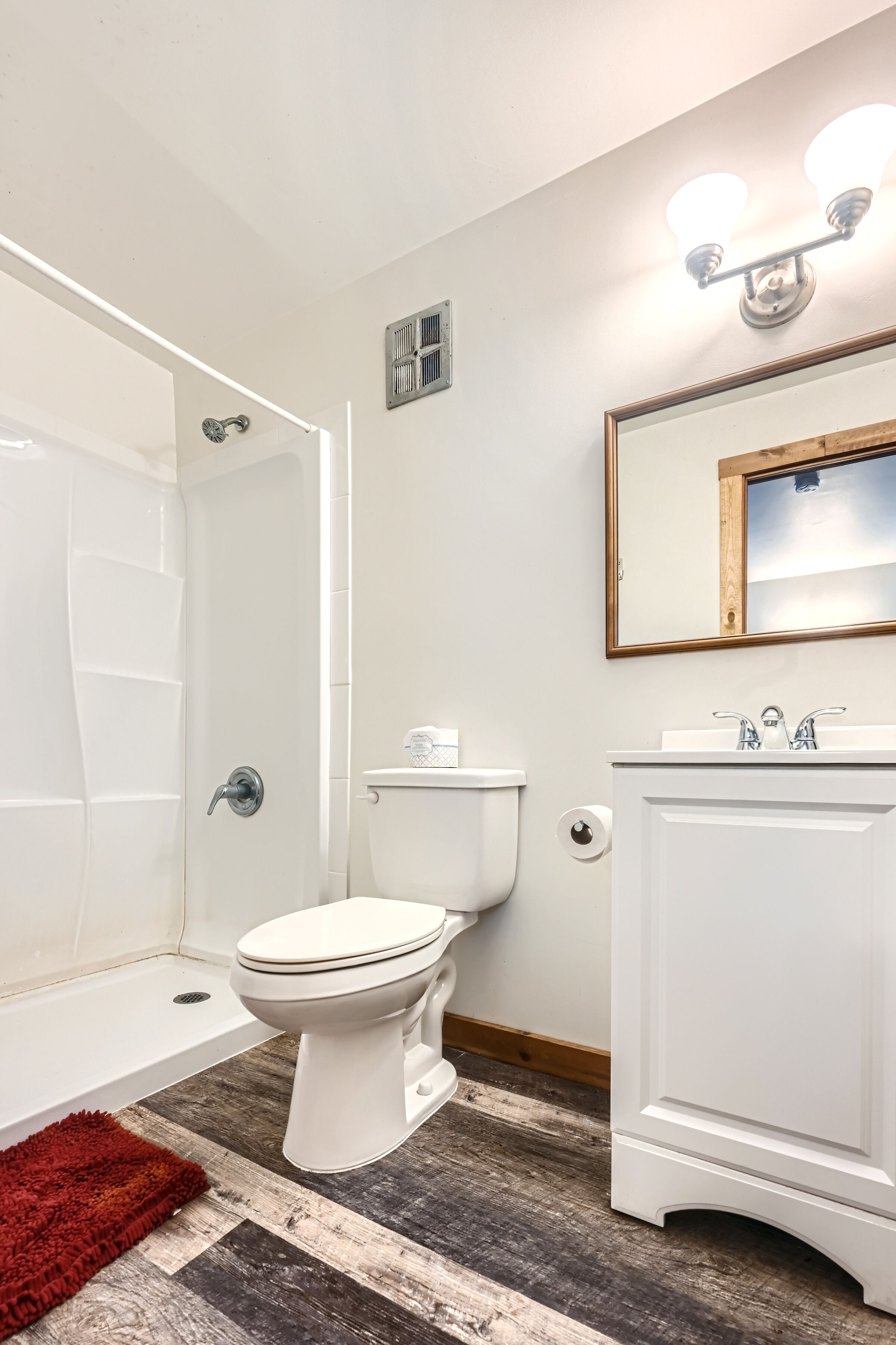 Un baño con inodoro y lavamanos blancos, un espejo y una ducha.