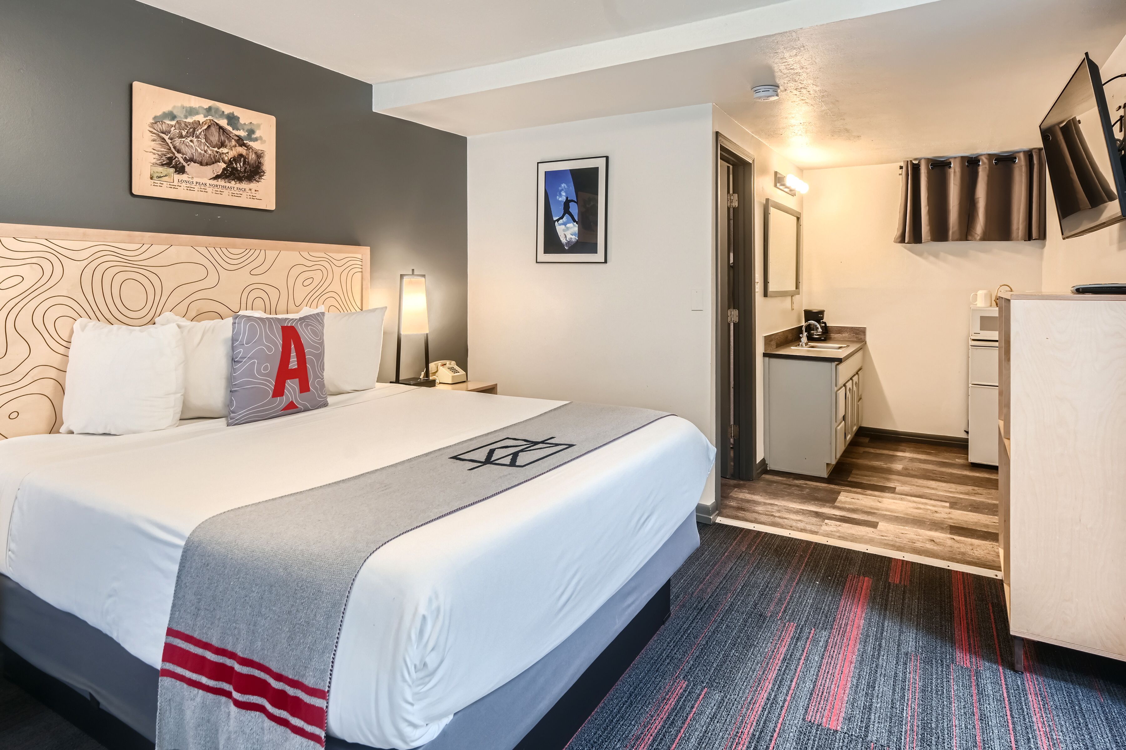 A hotel room with a large bed, a desk, a chair, a mirror, and a picture on the wall.