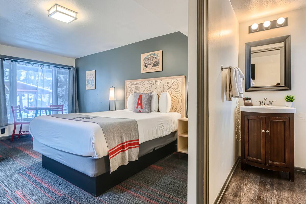 Une chambre d’hôtel avec un lit, une table de chevet, une lampe et une vue sur l’extérieur.