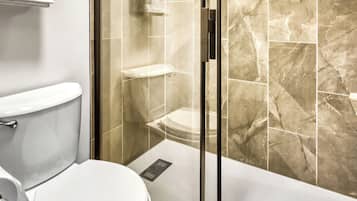 A modern bathroom with a glass-enclosed shower, a toilet, and a marble-tiled wall.