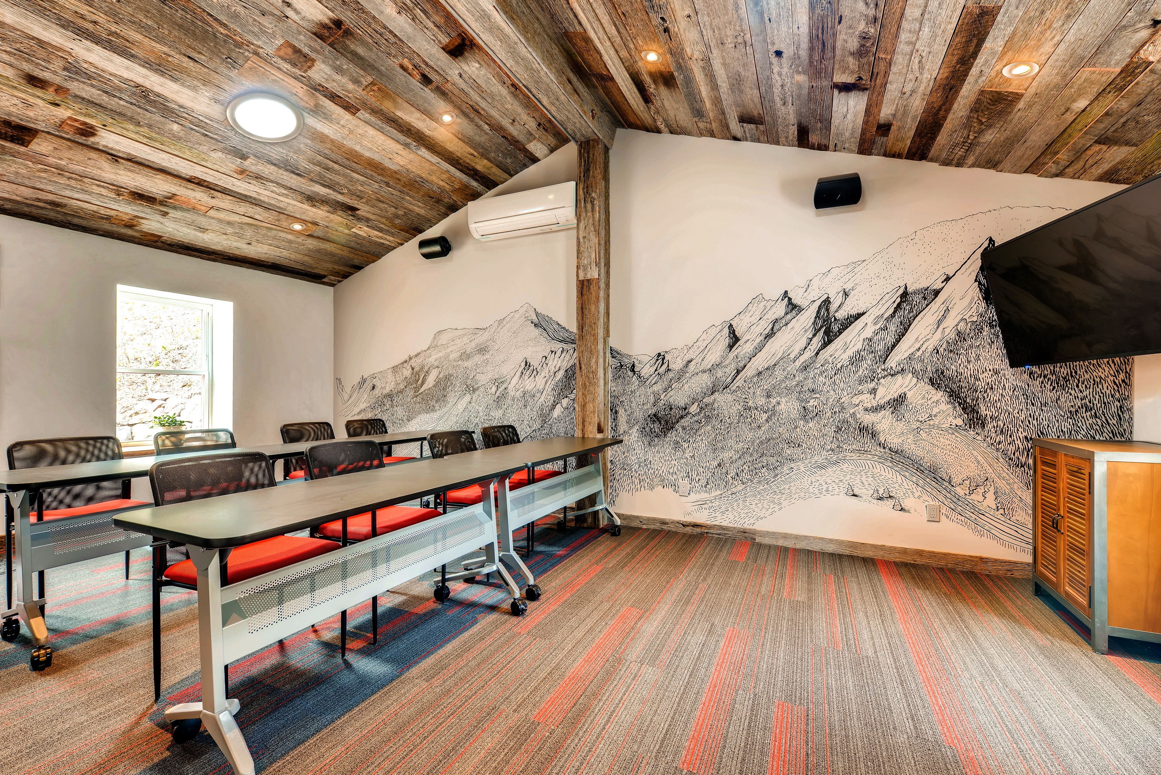 A conference room with a long table, chairs, and a mural of mountains.