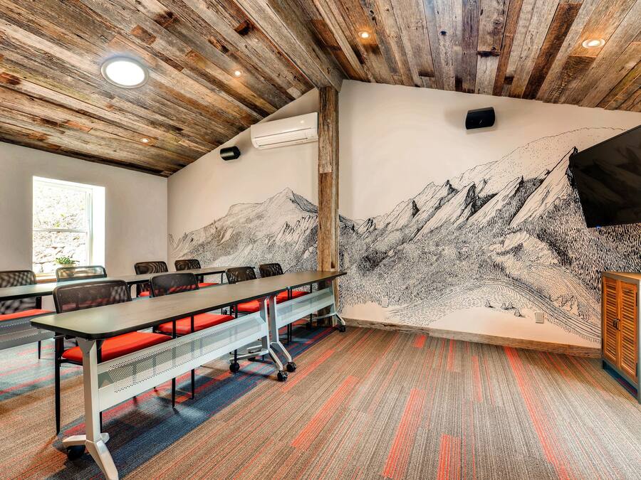 Uma sala de conferência com uma mesa comprida, cadeiras e um mural de montanhas.